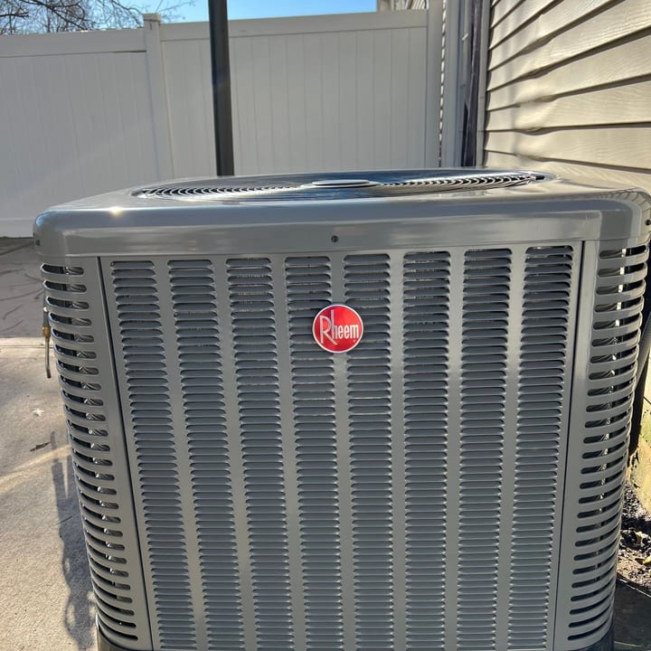 Rheem central air condenser installed beside a vinyl privacy fence