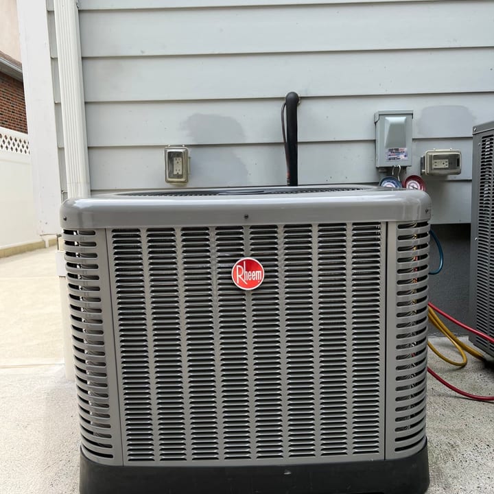 Rheem condenser installed on a pad against the side of a house