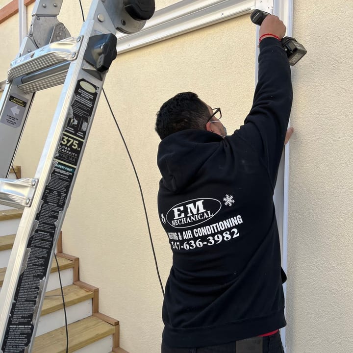 EM Mechanical technician on a ladder fitting line-set covers to an exterior wall