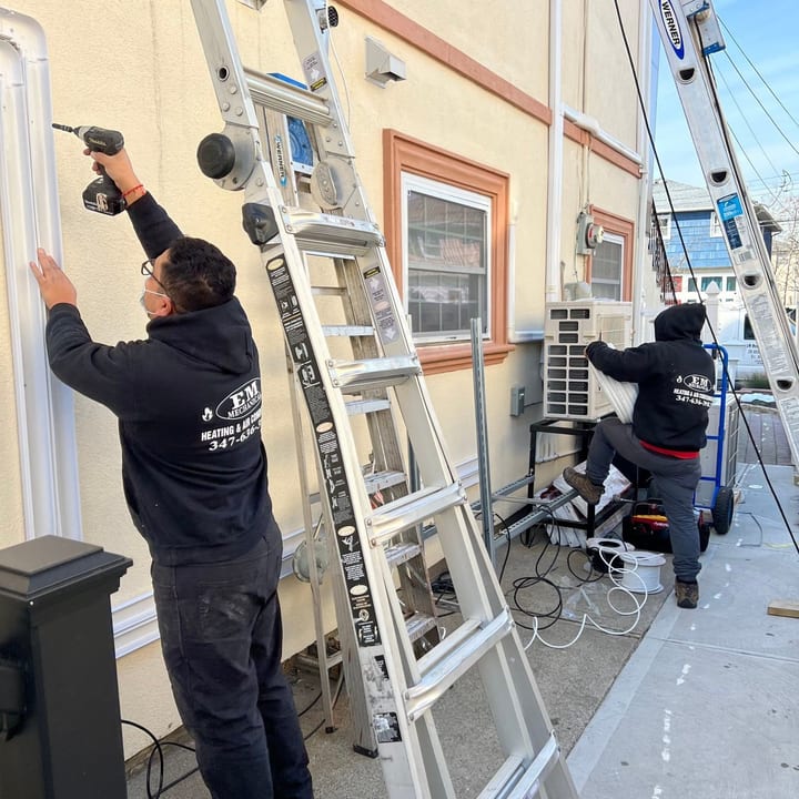 Two technicians on ladders installing line-set covers along a house exterior