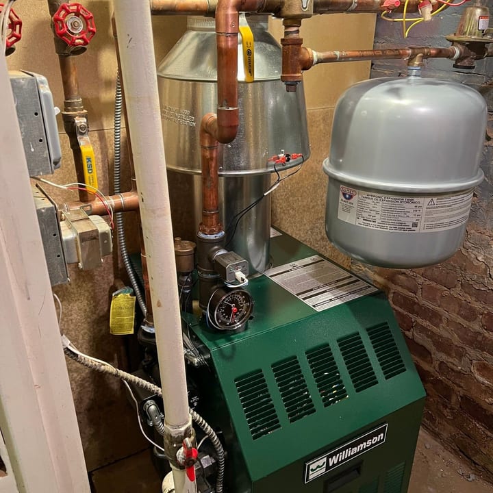 Green cast-iron boiler with copper piping and an expansion tank in a basement