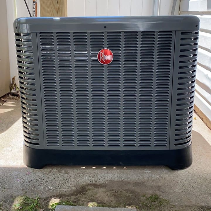 Rheem condenser installed on a pad beside a lattice fence