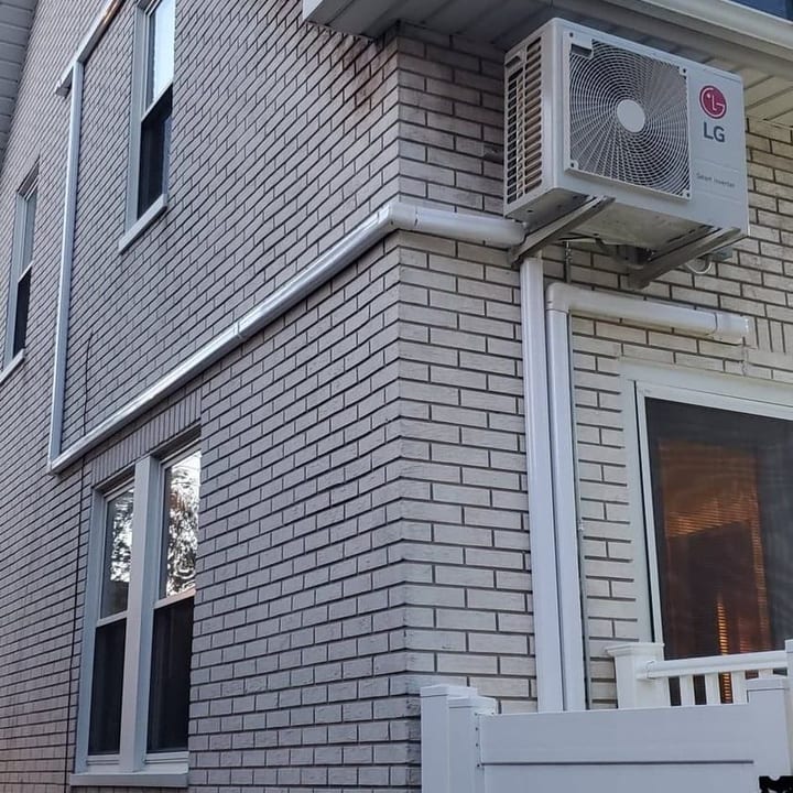 Mini-split outdoor unit wall-mounted on a grey-shingled home
