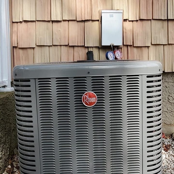 Rheem condenser installed on a gravel pad beside cedar shingles